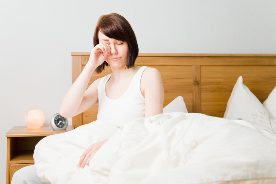 Young woman rubbing her eyes as she wakes up in her bed